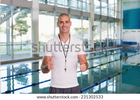 Portrait of a swimming coach gesturing thumbs up by the pool at leisure center