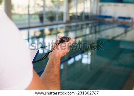 Close up of a cropped swimming coach with stopwatch by the pool at leisure center