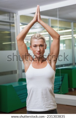 Portrait of a sporty young woman with joined hands over head at fitness studio