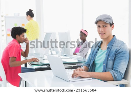 Young creative man using laptop at desk in creative office