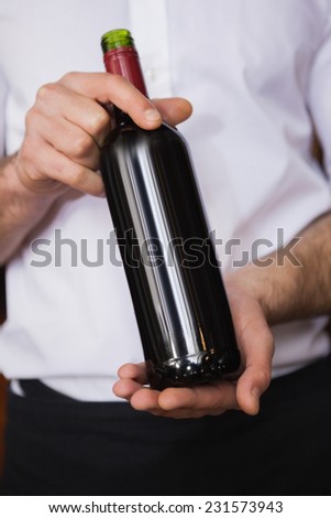 Handsome waiter holding a bottle of red wine in a bar