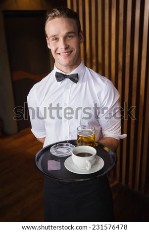 Smiling waiter holding tray with coffee cup and pint of beer in a bar