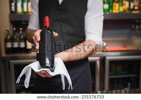 Handsome waiter holding a bottle of red wine in a bar