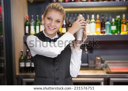 Pretty blonde waitress shaking cocktail in a bar
