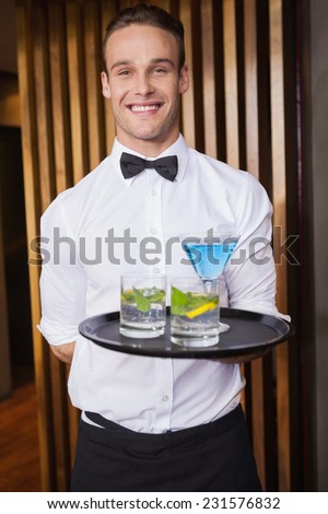 Cheerful young waiter holding tray with cocktails in a bar