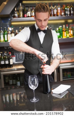 Handsome waiter opening a bottle of red wine in a bar