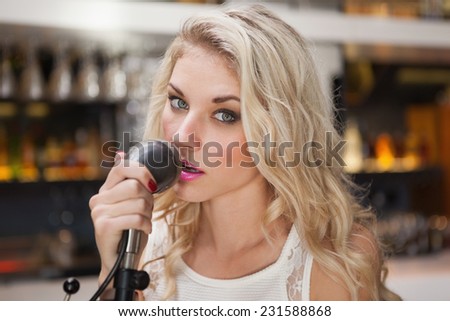 Young blonde woman singing while looking at camera at the nightclub