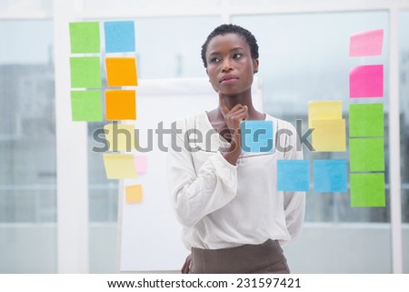 Creative businesswoman looking at sticky notes on window in the office