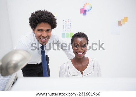 Smiling coworker using computer and looking at camera in the office