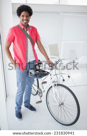 Smiling businessman standing with his bike in his office