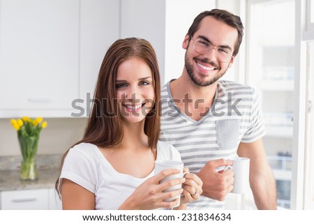 Young couple smiling at the camera having coffee at home in the kitchen