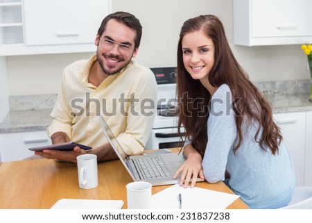 Young couple smiling at camera using technology at home in the kitchen