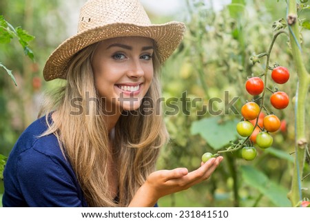 Pretty blonde looking at tomato plant at home in the garden