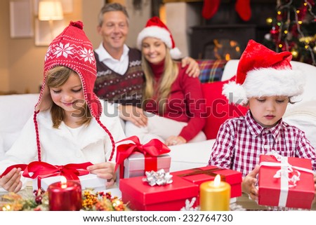 Festive little siblings opening a gift in front of their parents at home in the living room