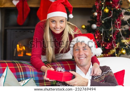 Happy woman offering husband a gift at home in the living room