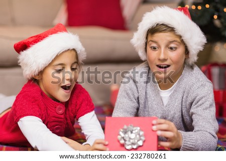 Shocked brother and sister opening a gift at home in the living room