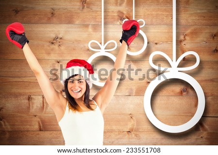 Festive brunette in boxing gloves cheering against christmas decorations over wood