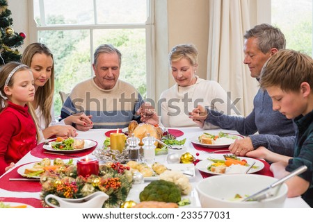 Extended family saying grace before christmas dinner at home in the dining room