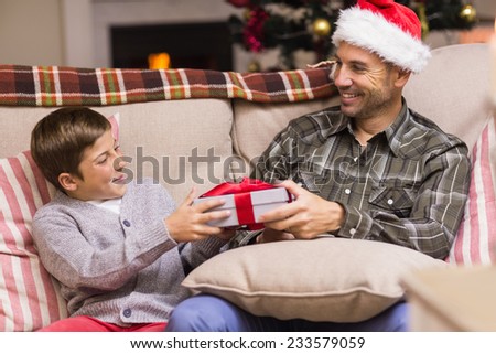 Son giving father a christmas gift on the couch at home in the living room