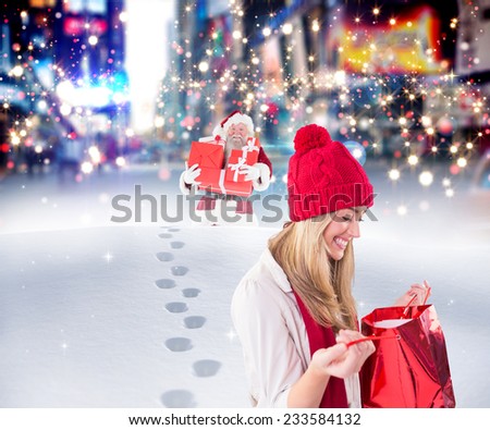 Happy blonde opening gift bag against santa delivering gifts in city