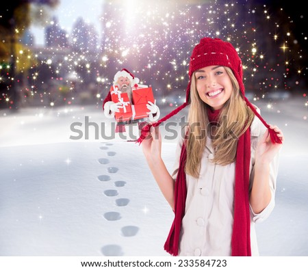 Pretty blonde smiling at camera in warm clothes against santa delivering gifts in city