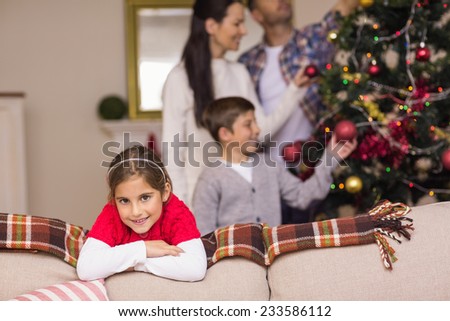 Cute girl leaning on the couch while her family decorating the christmas tree