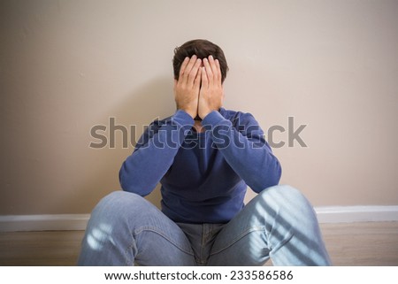Depressed man sitting on floor in an empty room