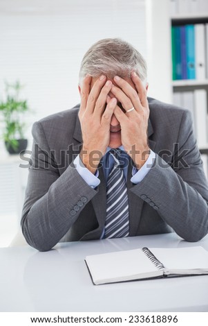 Stressed businessman covering his face in his office