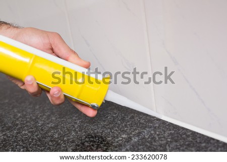 Plumber putting filling in between tiles in the kitchen