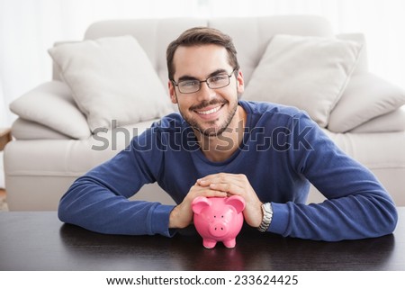 Smiling young man with piggy bank at home in the living room