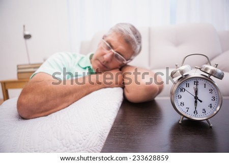 Man dozing on the couch beside alarm clock at home in the living room