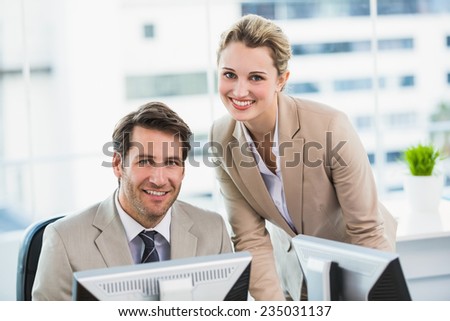 Smiling businessman helping his colleague at a computer at work