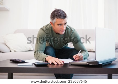 Concentrated man using laptop and taking notes at home in the living room