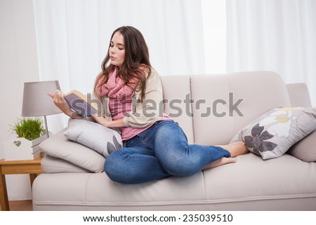 Pretty brunette reading book on couch at home in the living room