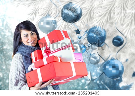 Smiling brunette holding pile of gifts against christmas tree branch with blue decorations