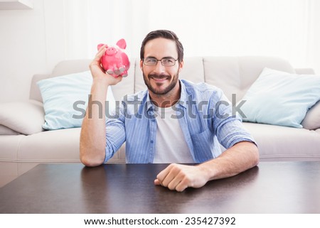 Happy man shaking a pink piggy bank in the living room