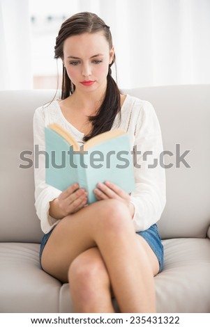 Pretty brunette reading book on couch at home in the living room