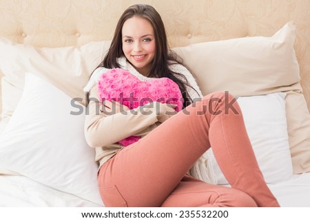 Pretty brunette holding heart cushion on bed at home in the bedroom