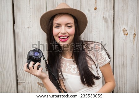 Pretty brunette holding her camera against bleached wooden planks