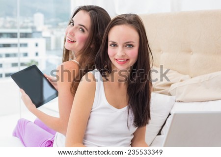 Pretty friends using their technology on bed at home in the bedroom