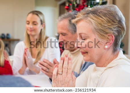 Extended family saying grace before christmas dinner at home in the dining room