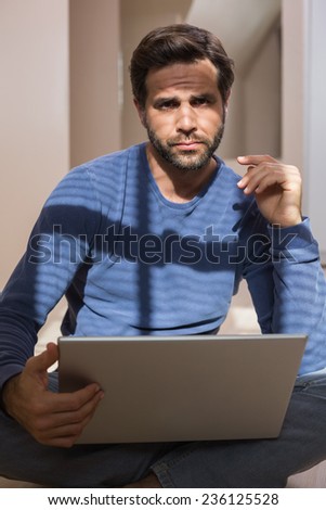Depressed man sitting on floor using laptop in an empty room