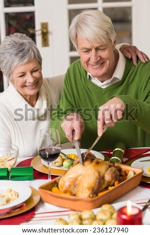 Man carving chicken while his wife having arm around him at home in the living room