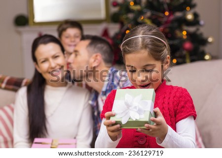 Surprised little girl opening a gift in front of her family at home in the living room