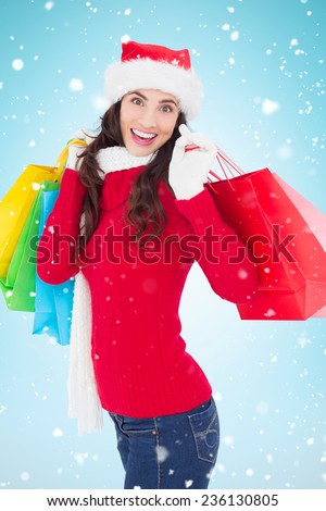 Festive brunette in winter wear holding shopping bags against blue background with vignette