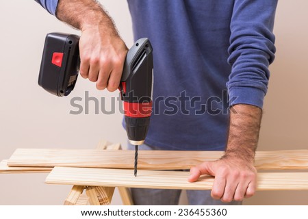 Casual man drilling hole in plank at home in the living room