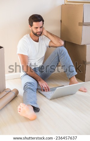 Happy man using laptop surrounded by boxes in his new home