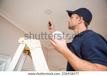 Handyman installing smoke detector with screwdriver on the ceiling