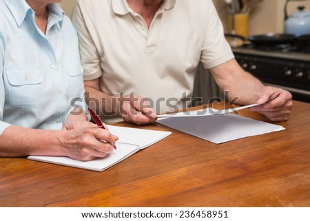 Senior couple reading and writing at home in the kitchen