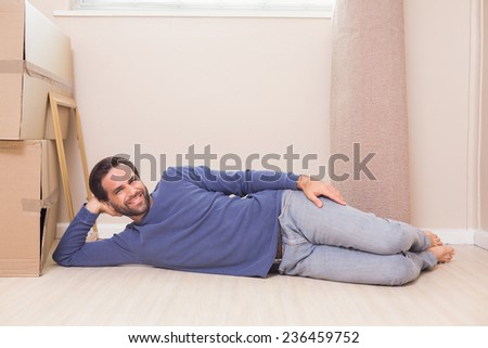 Happy man lying on floor with moving boxes in his new home